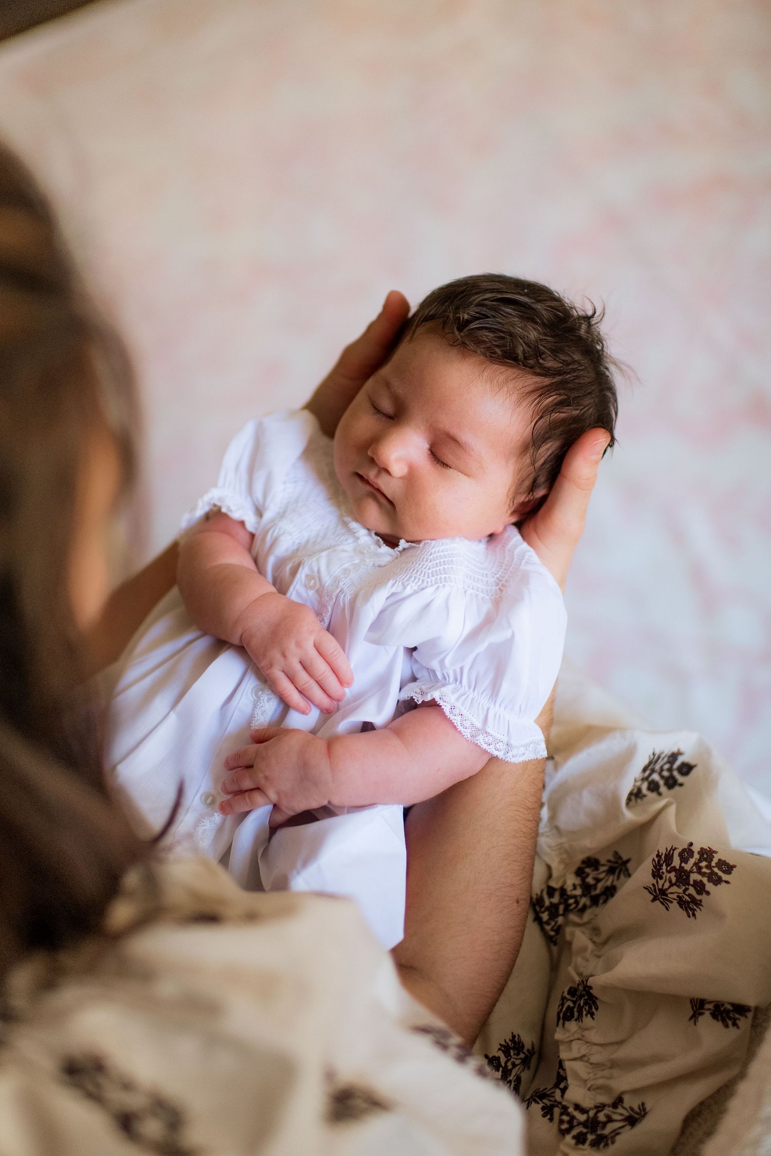 Close-up shots of a sleeping baby in white clothing being held against floral patterned fabric.
