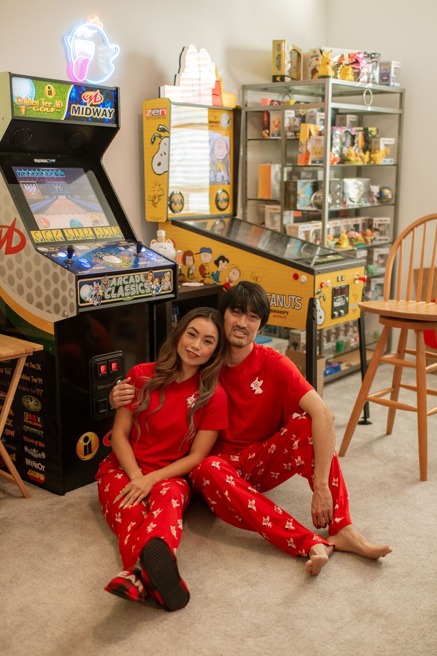 Couple in matching red pajamas relaxing in game room with arcade machines.