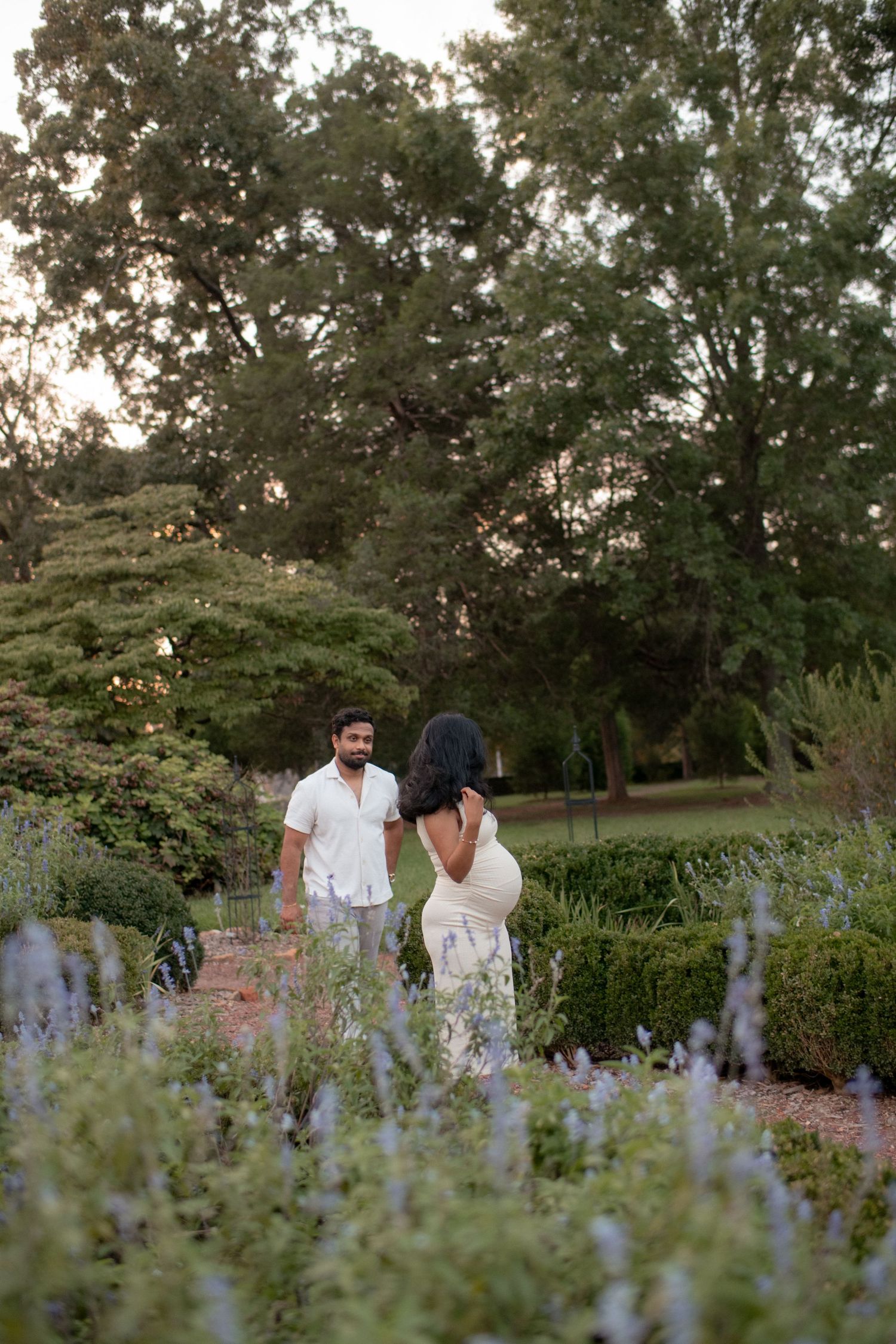 Couple walking through garden with blooming purple flowers during sunset.
