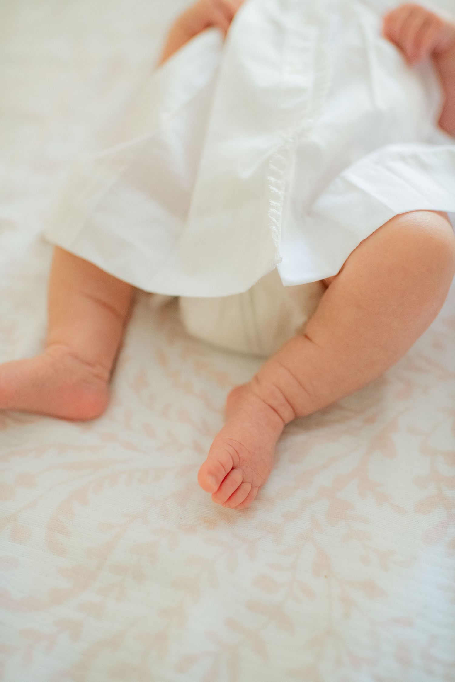 Close-up details of tiny baby feet and white dress against soft bedding.