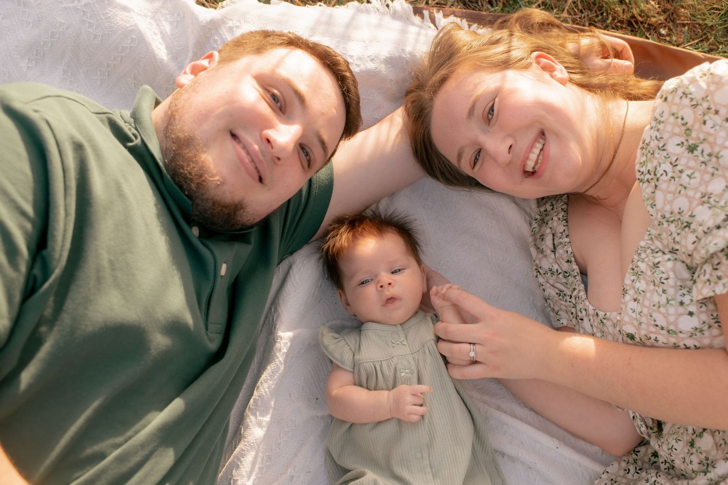 A happy family lying down together on a white surface outdoors during a sunny day.