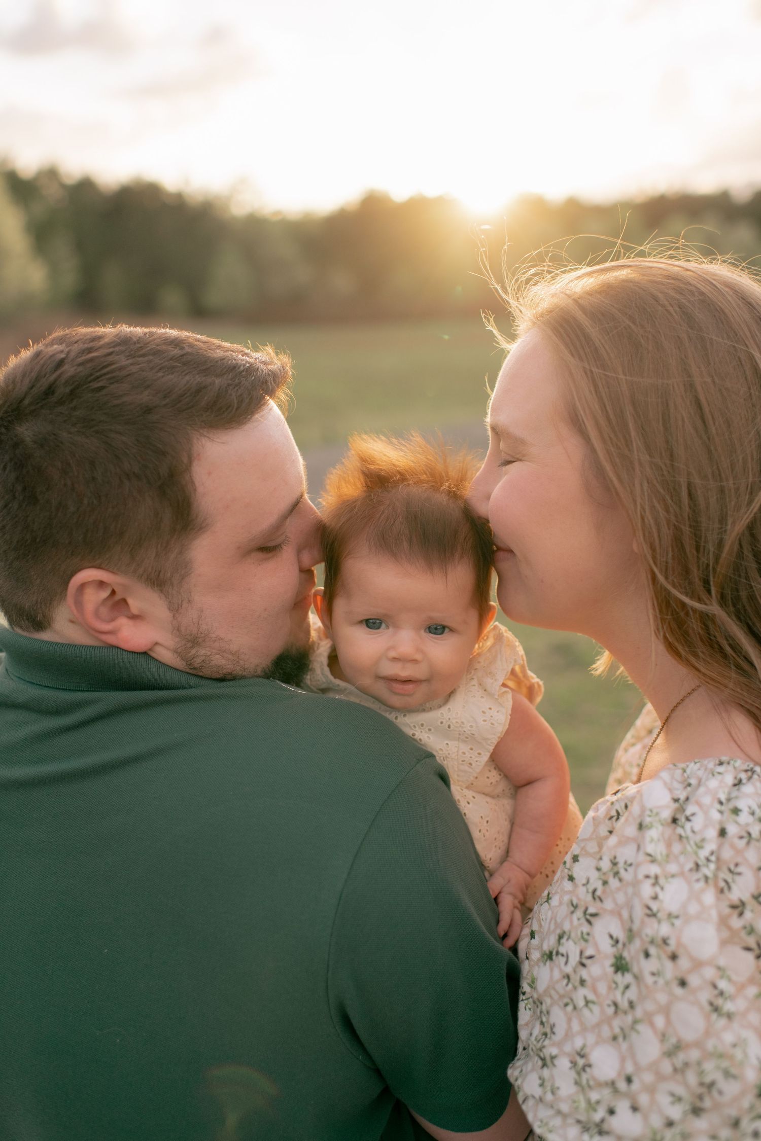 A family shares an intimate moment together in a golden sunset-lit field, wearing casual clothes in earth tones.