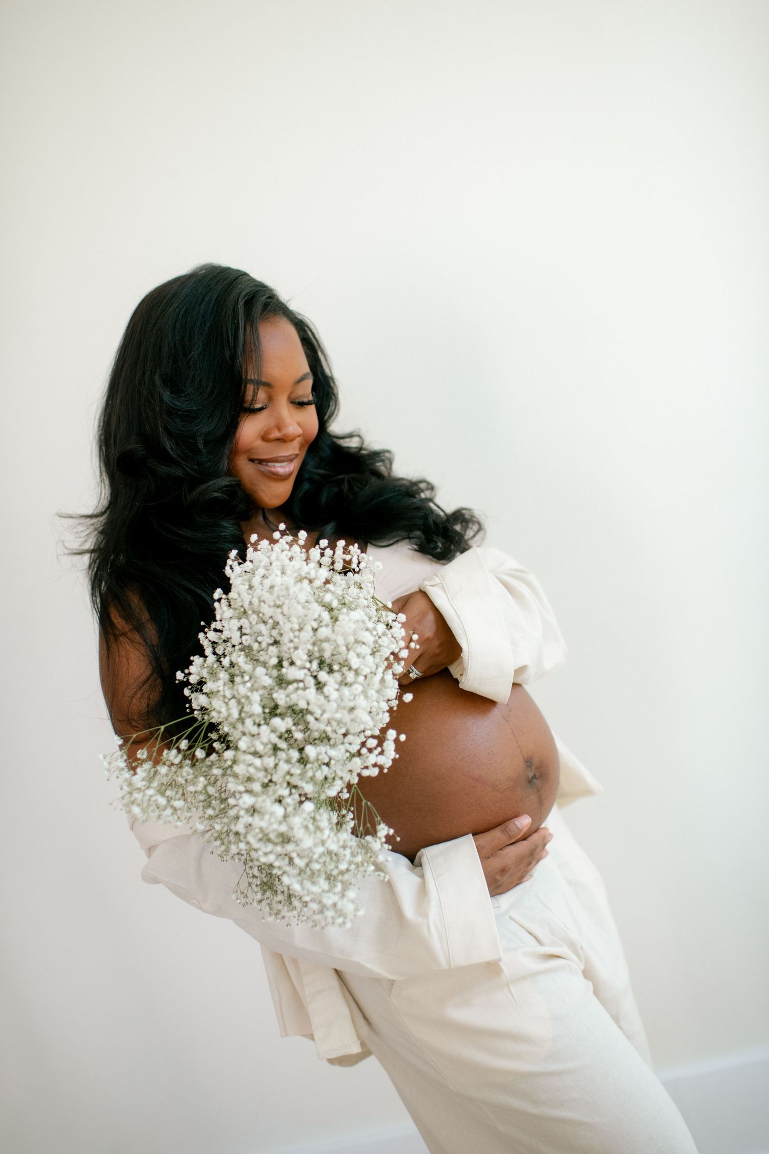 Ethereal maternity portraits with baby's breath flowers and flowing white fabric against light background.