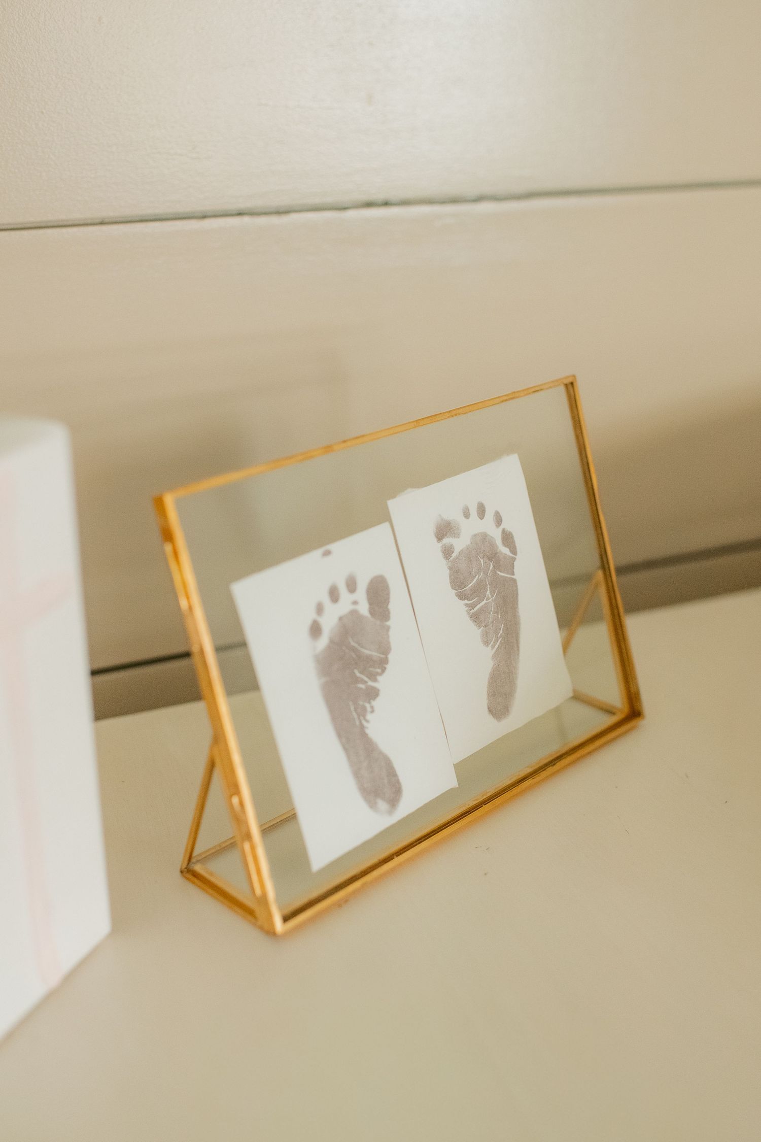 Baby footprints displayed in a gold-framed glass frame on a white surface.