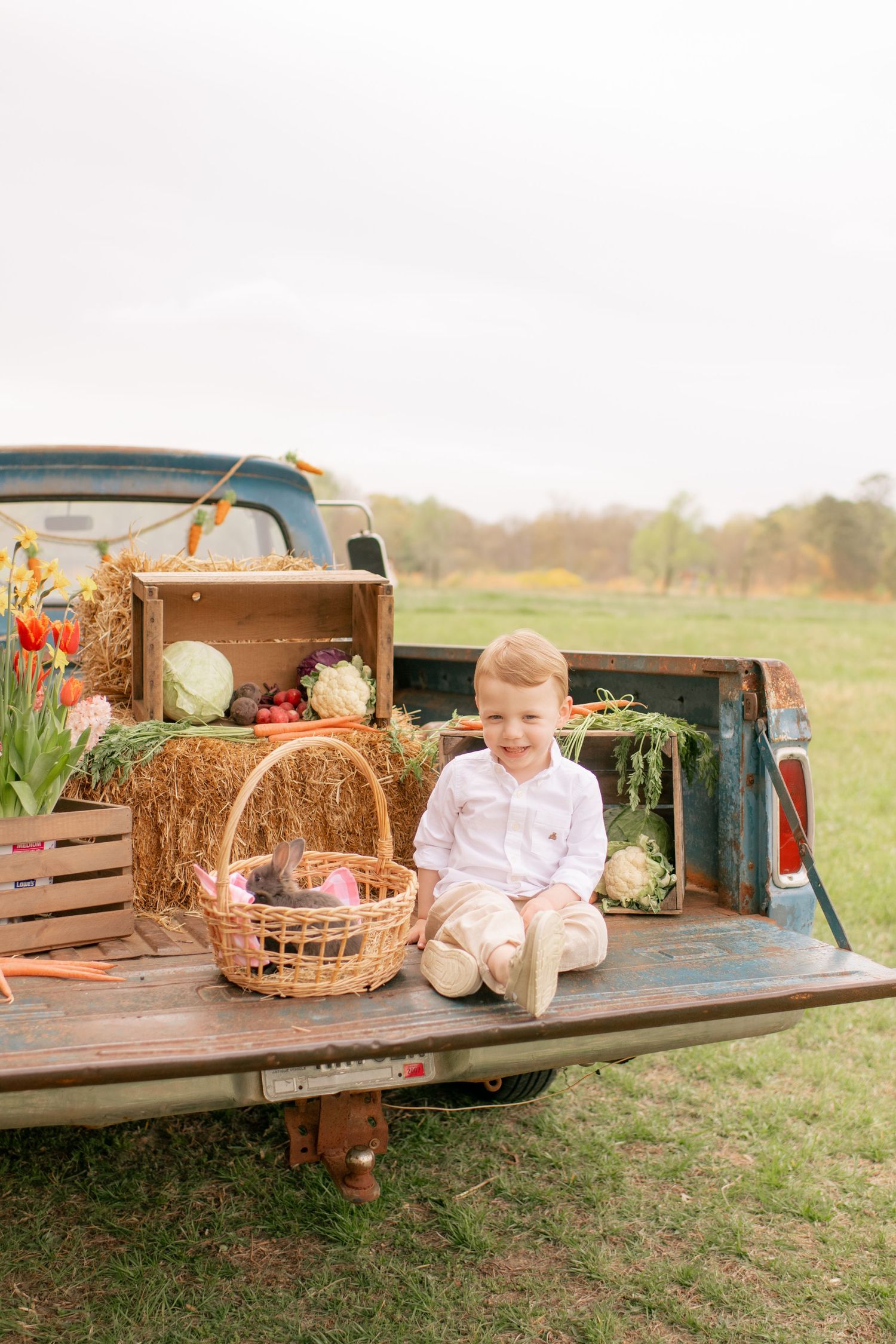 Rustic spring scene on vintage truck tailgate with hay bales, produce baskets and floral decorations in outdoor setting.