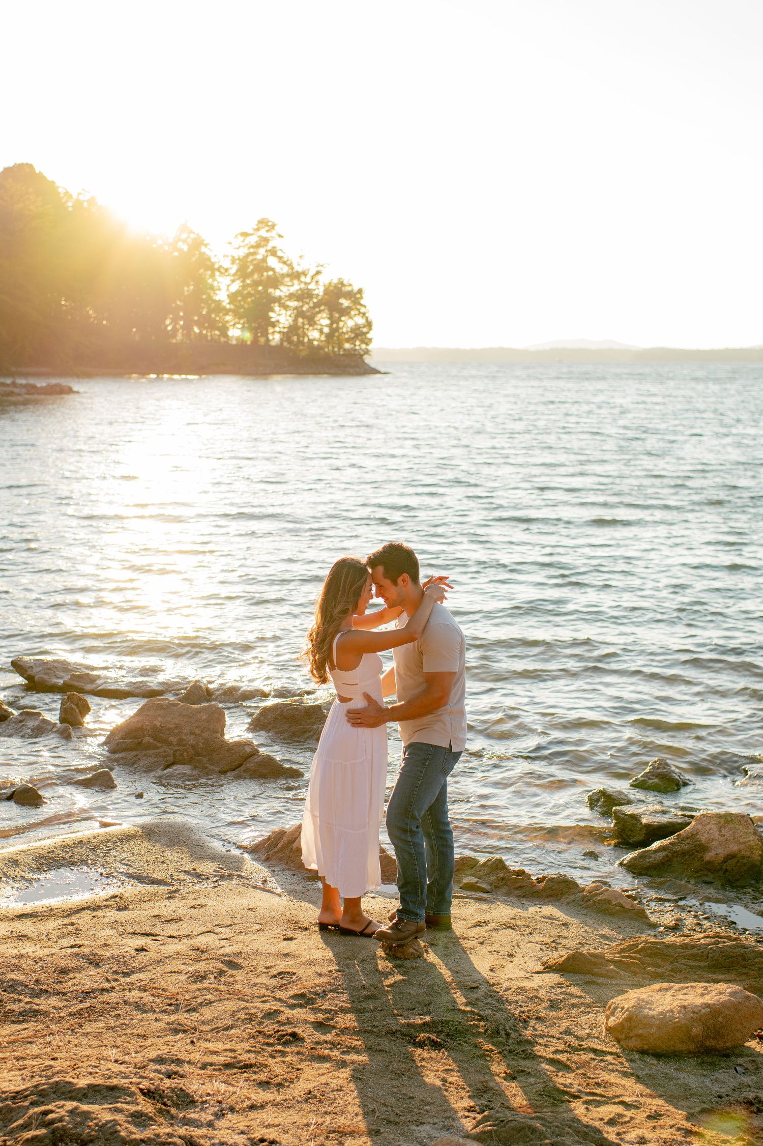 Romantic beach scene with couple embracing on rocky shore during golden hour.