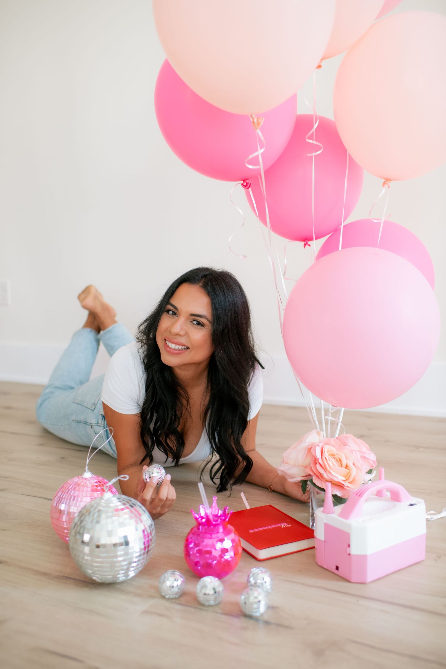 Person lying on floor with pink balloons and decorative silver disco balls.