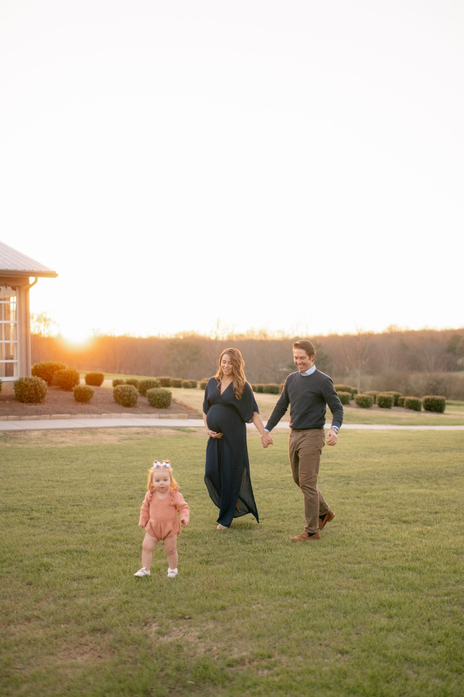 A family runs together on grassy property during golden sunset hour at a countryside venue.