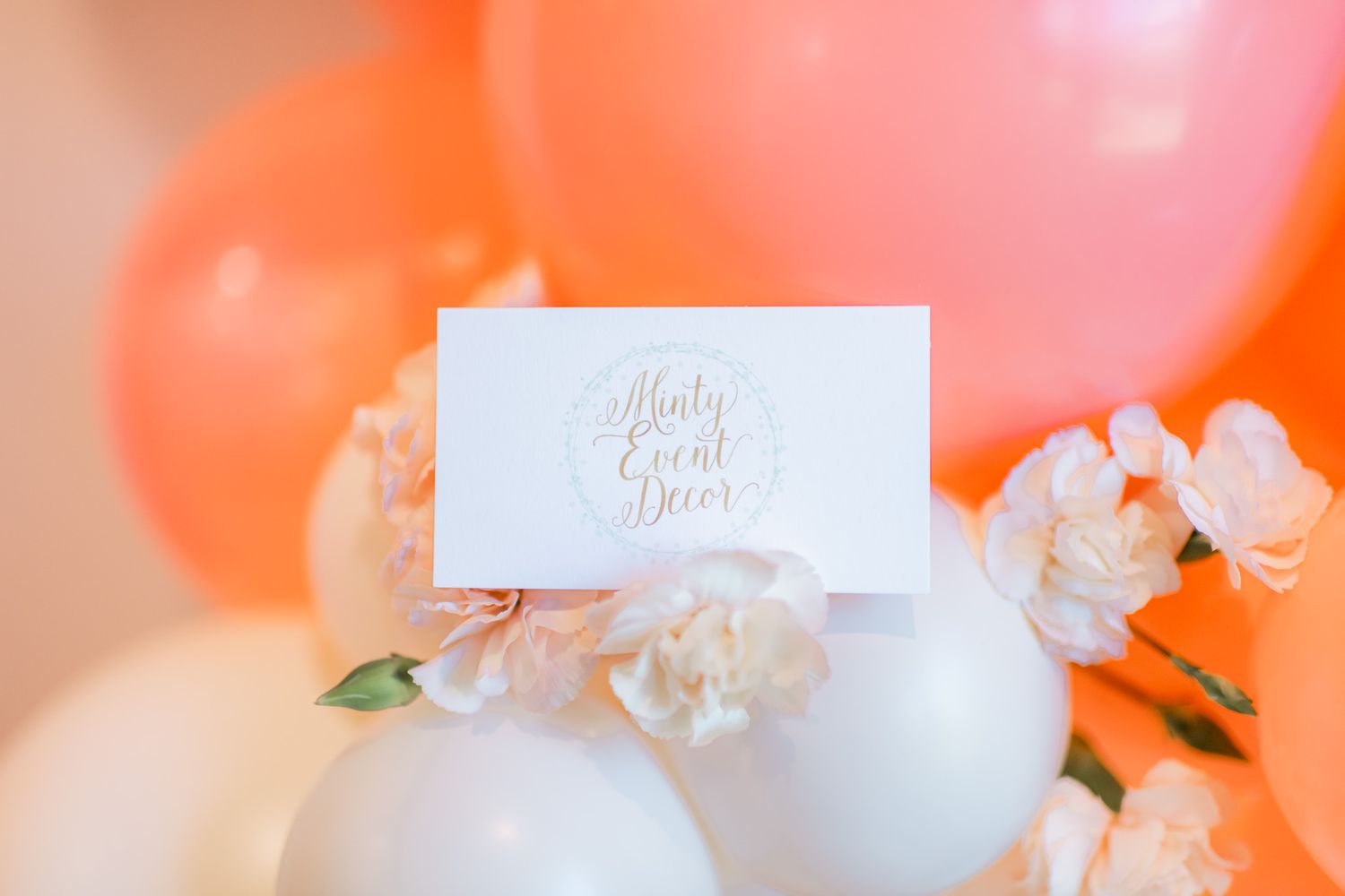 Colorful pink and orange balloon decorations create a festive backdrop with white place cards displayed in front.