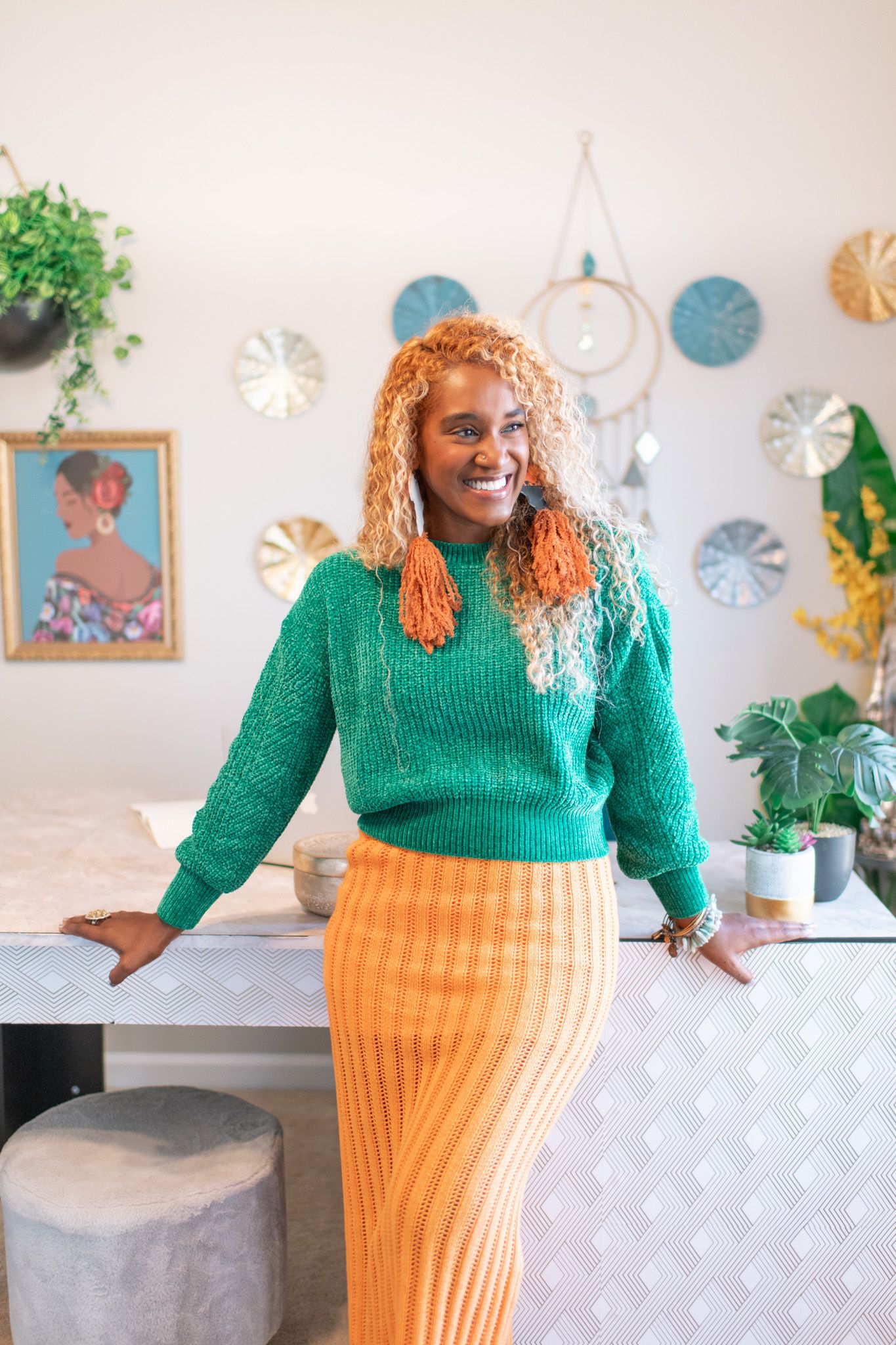 Person wearing green sweater and orange skirt poses in room with decorative wall art.