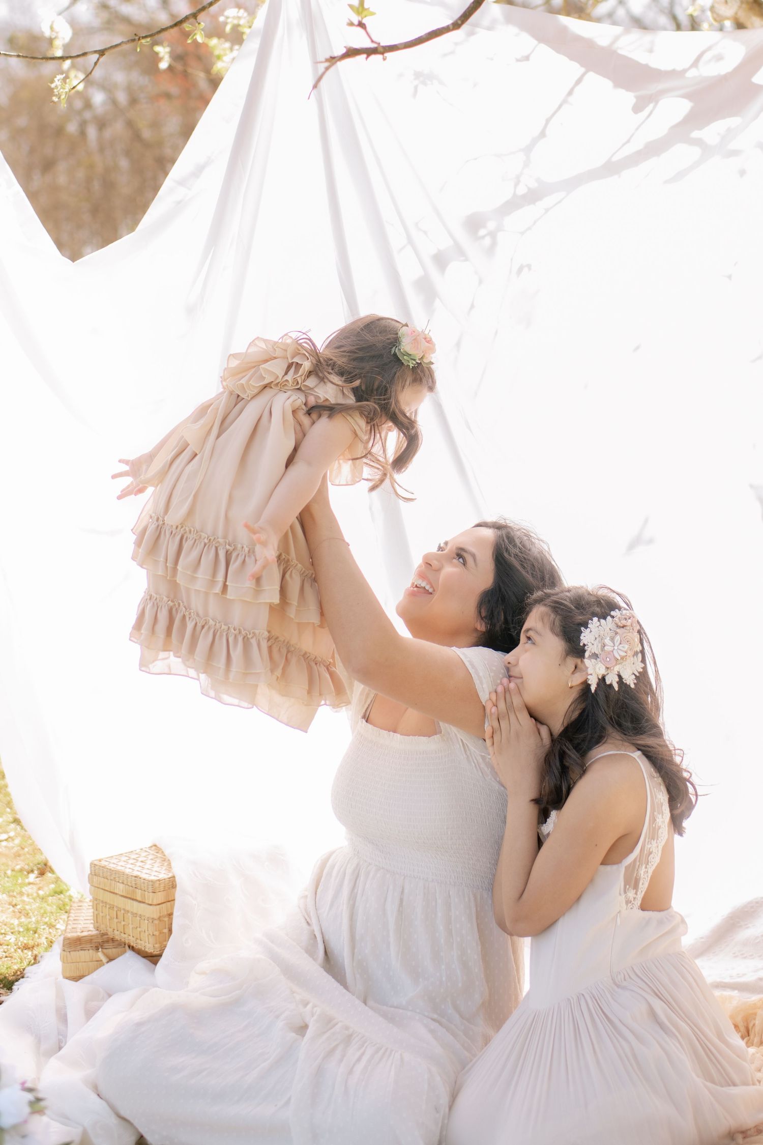 Two people in white dresses share a joyful moment together on a sunny day outdoors with flowy fabrics and soft lighting.