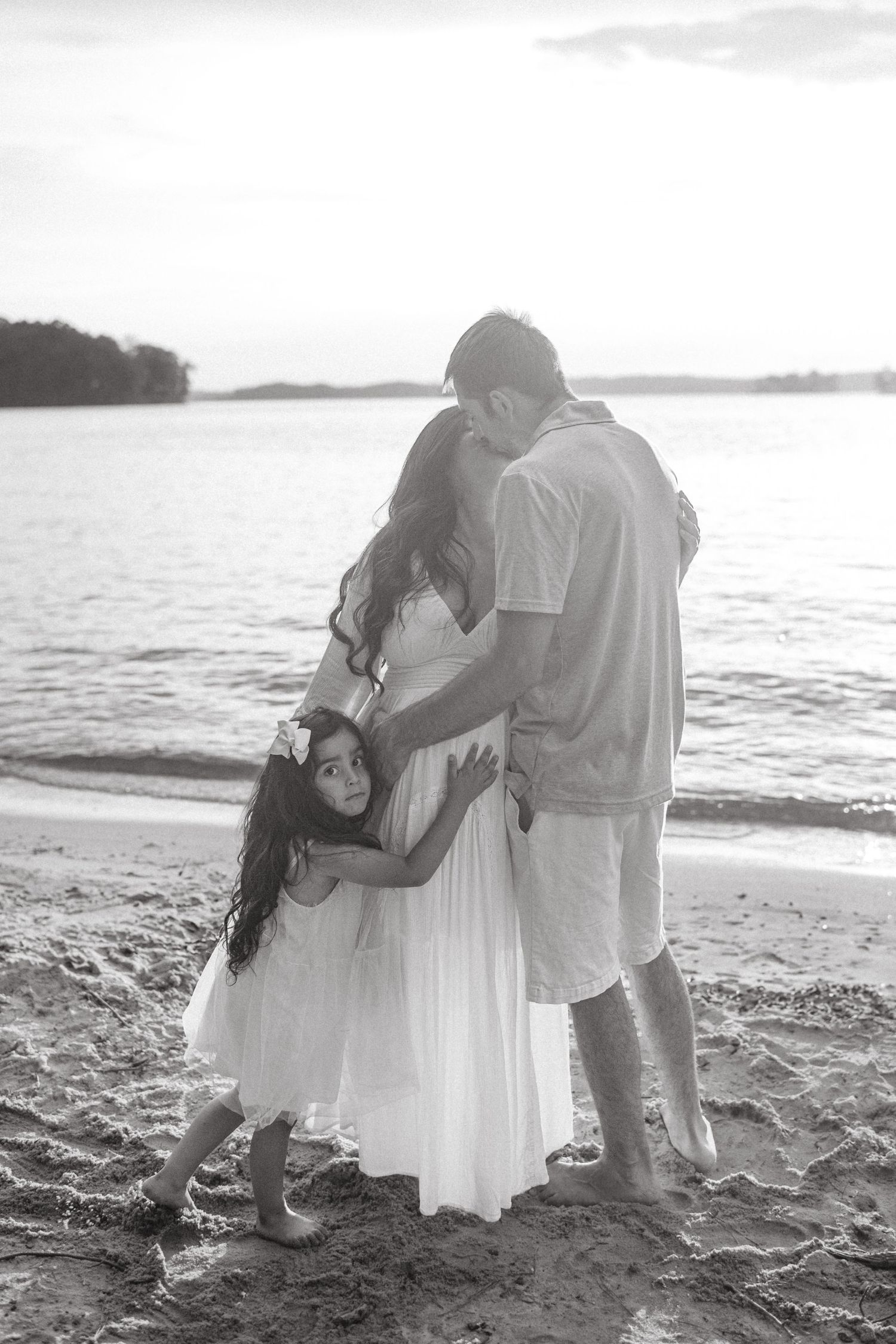 A family embraces together on a sandy beach at sunset in black and white.