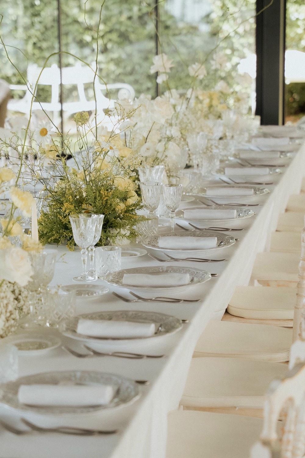 Elegant wedding reception table setting with delicate floral centerpieces and crystal glassware on white linens.