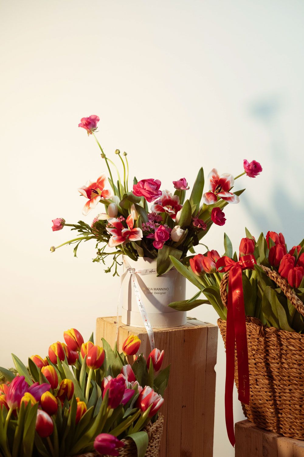 Colorful spring tulips and flowers arranged on wooden pedestals with woven baskets.