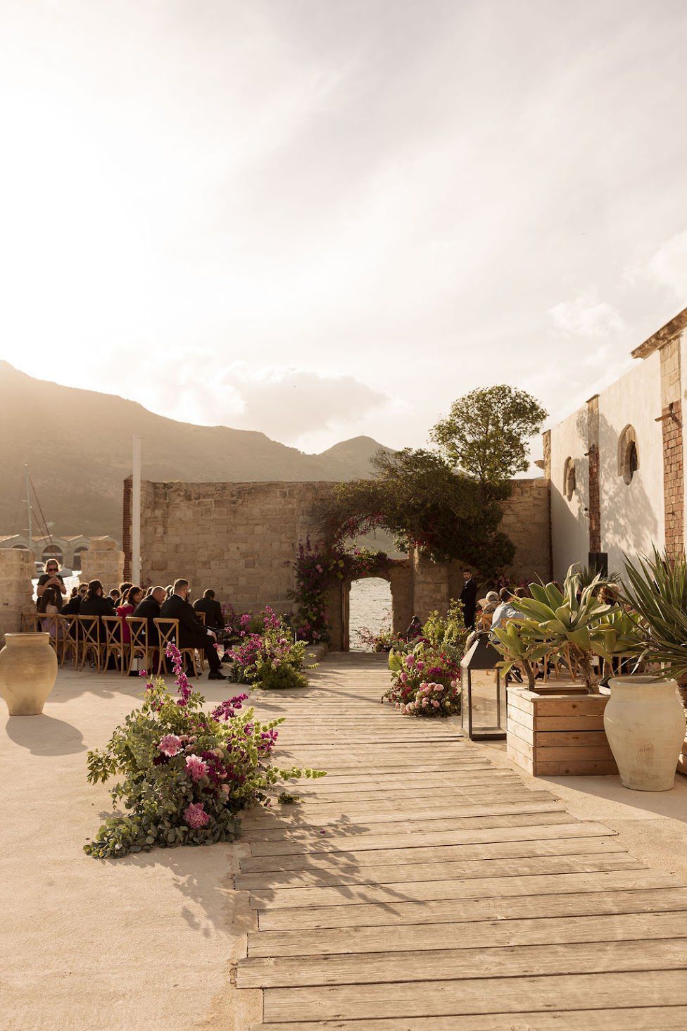 Panoramic view of a rustic outdoor terrace with stone steps and potted plants against a mountainous backdrop at sunset.