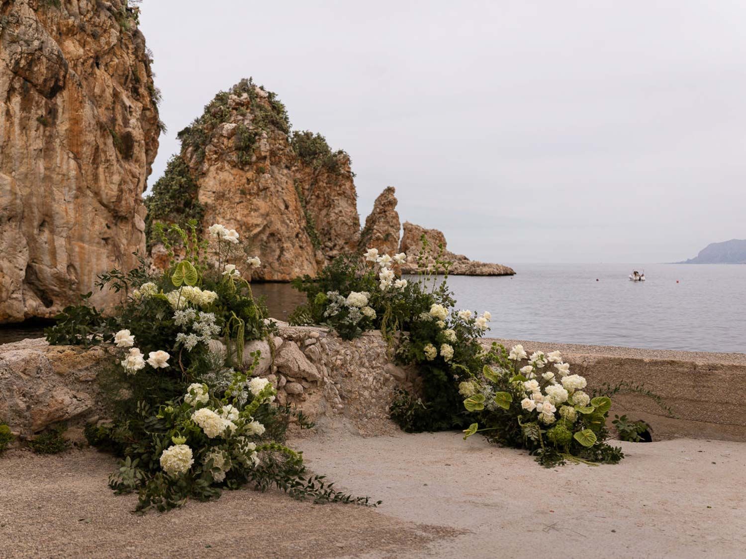 Coastal wedding decor with white floral arrangements against rocky cliffs.