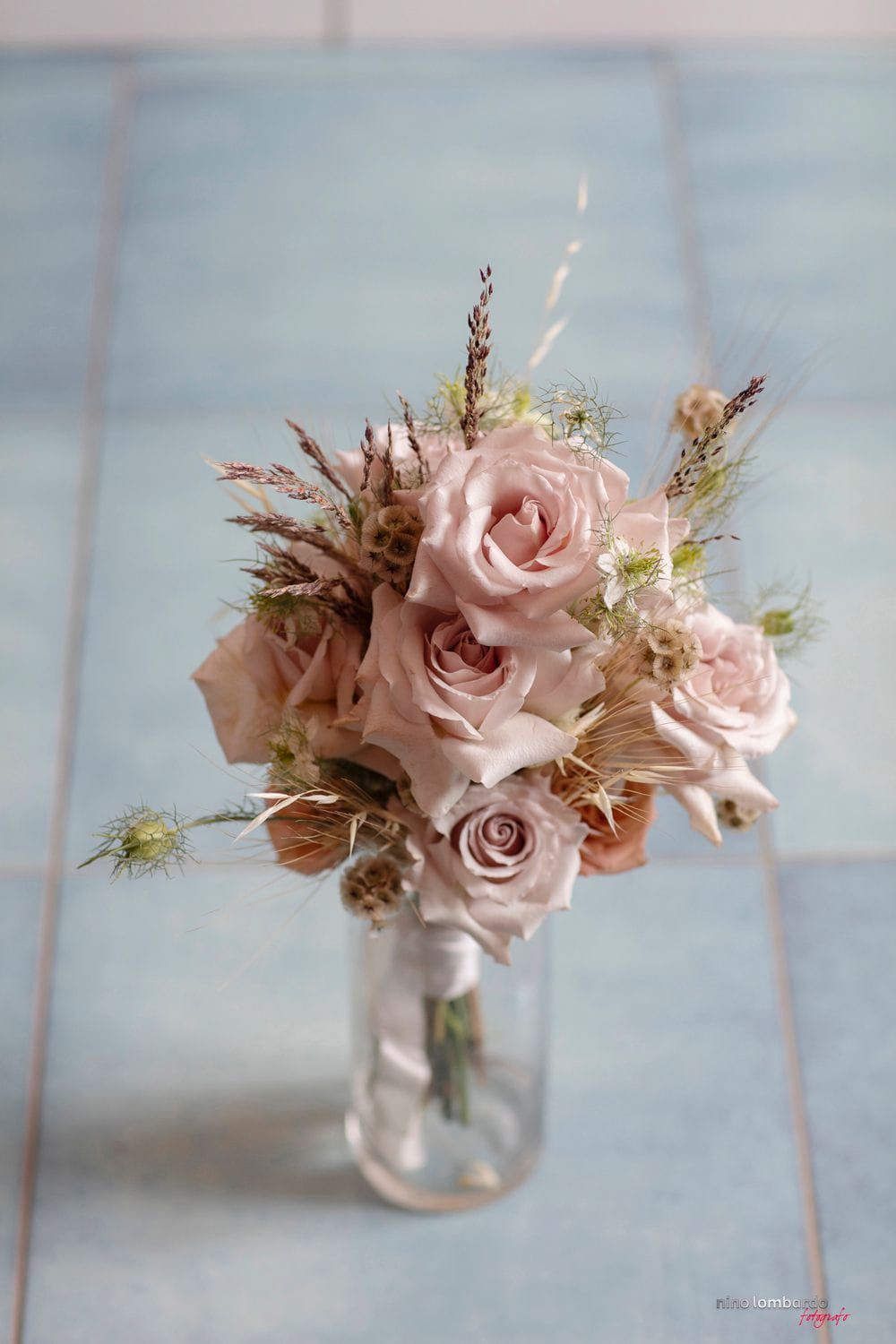 Delicate pink roses and dried flowers arranged in mason jars against a soft blue background.