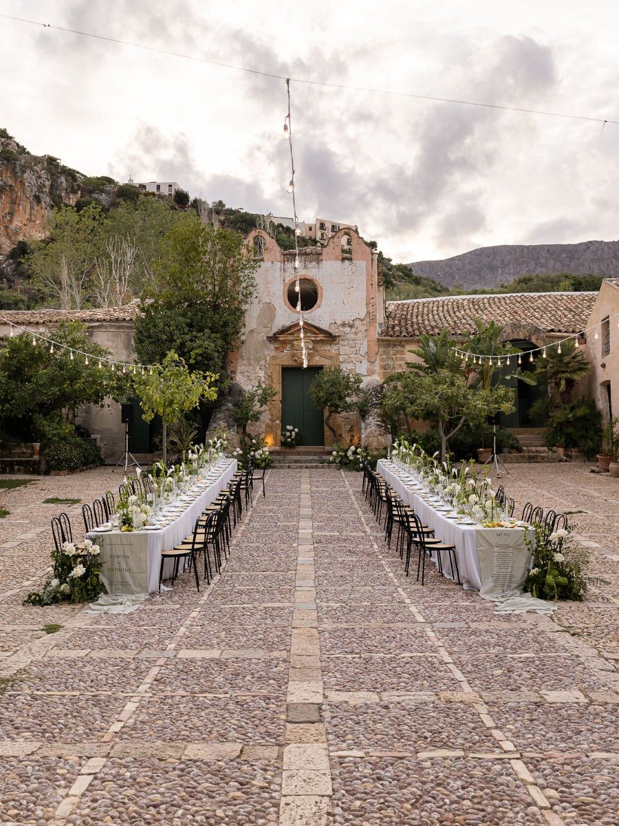 Rustic stone courtyard decorated for an outdoor wedding ceremony with white floral arrangements and string lights.