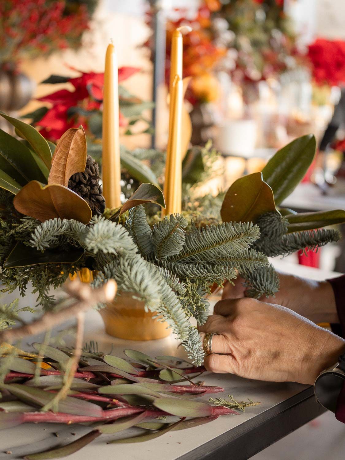 Close-up of hands arranging evergreen branches and gold candles for a holiday table setting.