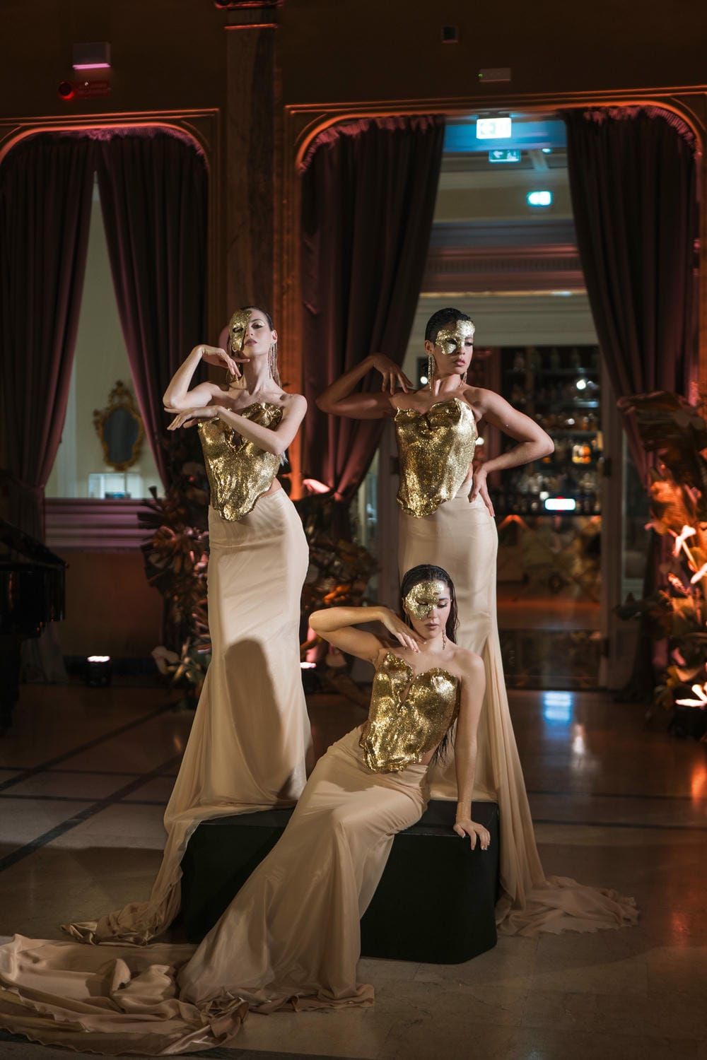 Hotel delle Palme Two performers in flowing white dresses and gold masks dance together on a dimly lit stage during an artistic performance.
