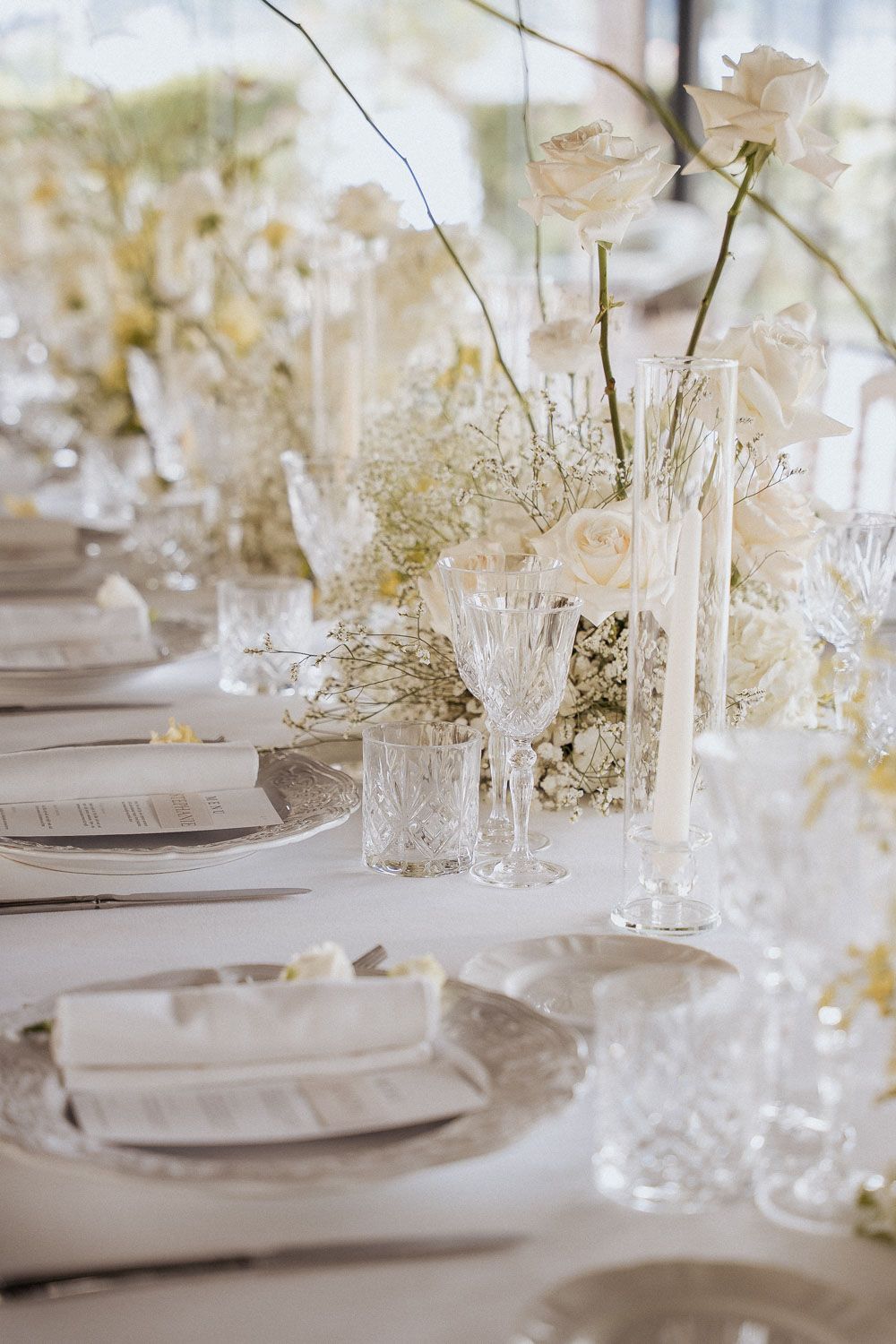 Elegant white wedding table settings with crystal glassware, delicate floral centerpieces and soft candlelight decor.