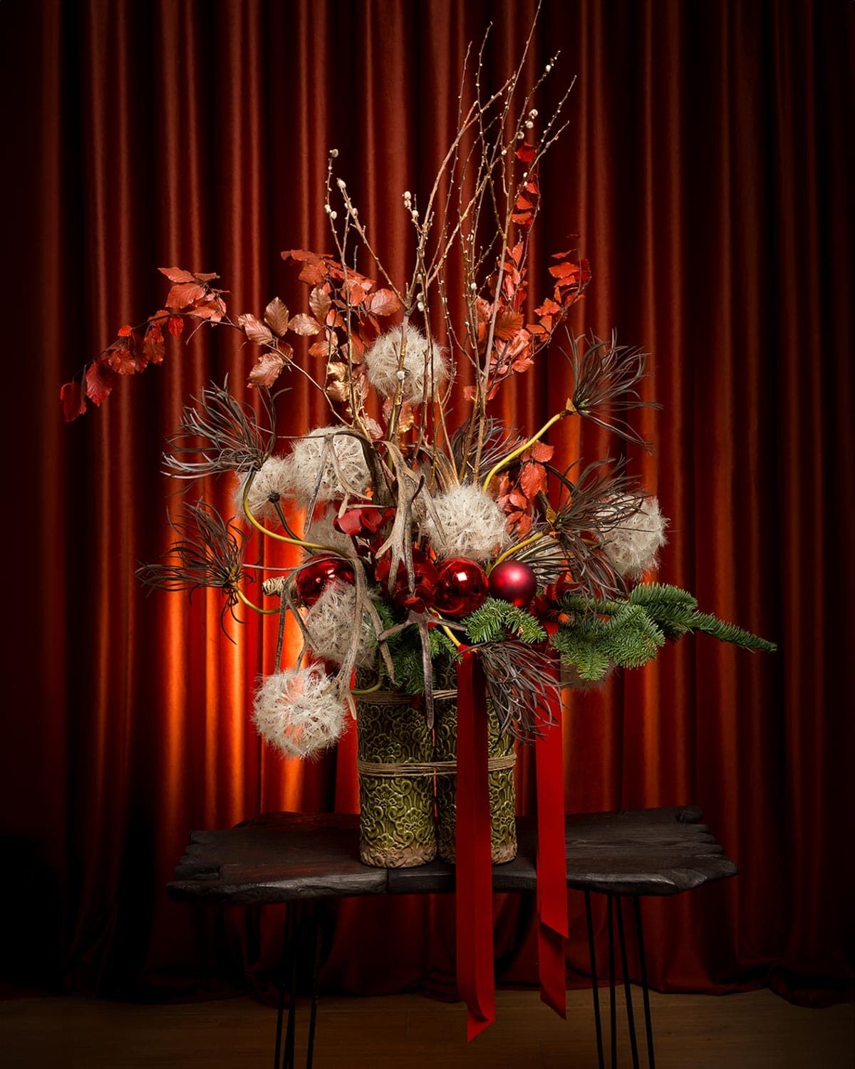 Elegant holiday floral arrangements with red accents displayed against a dramatic red curtain.
