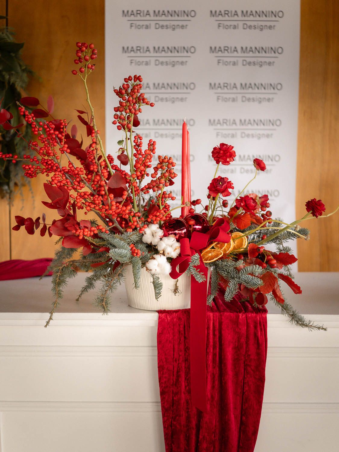 Elegant red floral arrangements displayed against a white backdrop with professional branding signage.