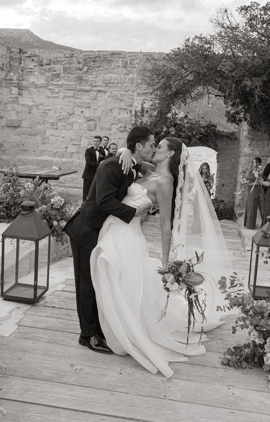 In Favignana a romantic black and white wedding photo showing a couple kissing during their outdoor ceremony with stone walls and lanterns.