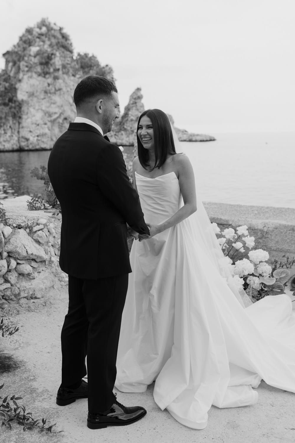 A romantic black and white wedding photo series showing a couple dancing together on a scenic coastal cliff, Scopello, Sicily.