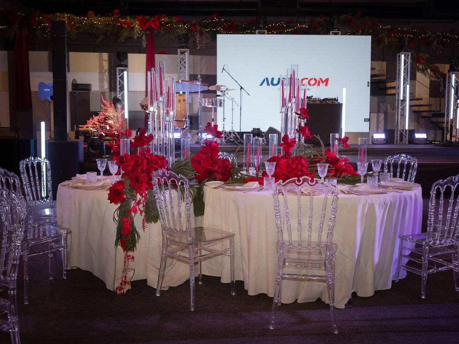 Elegant wedding reception venue with white tables, crystal centerpieces, and vibrant red floral arrangements.
