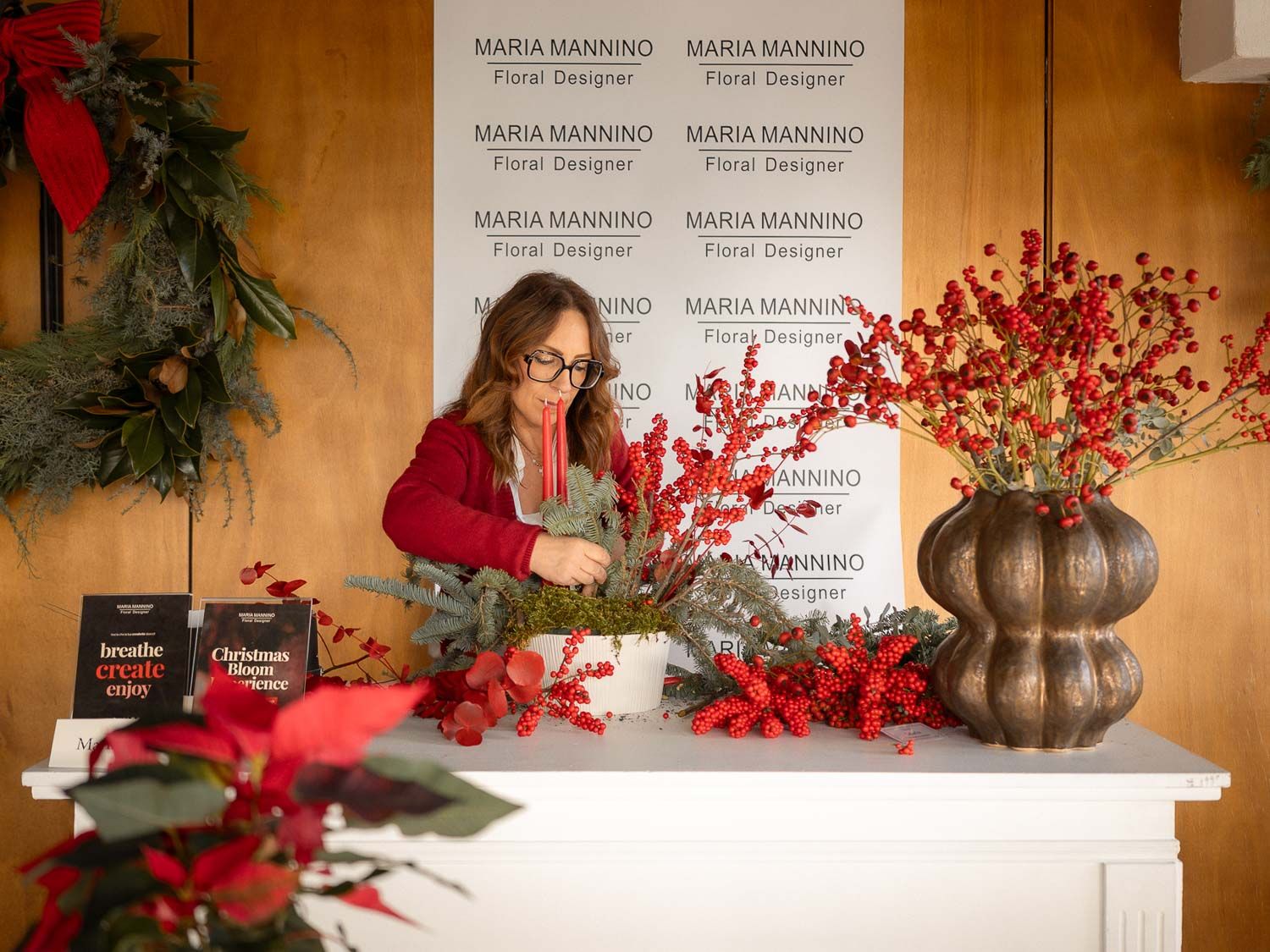 Professional floral design display featuring red berry arrangements and holiday decor against a branded backdrop.
