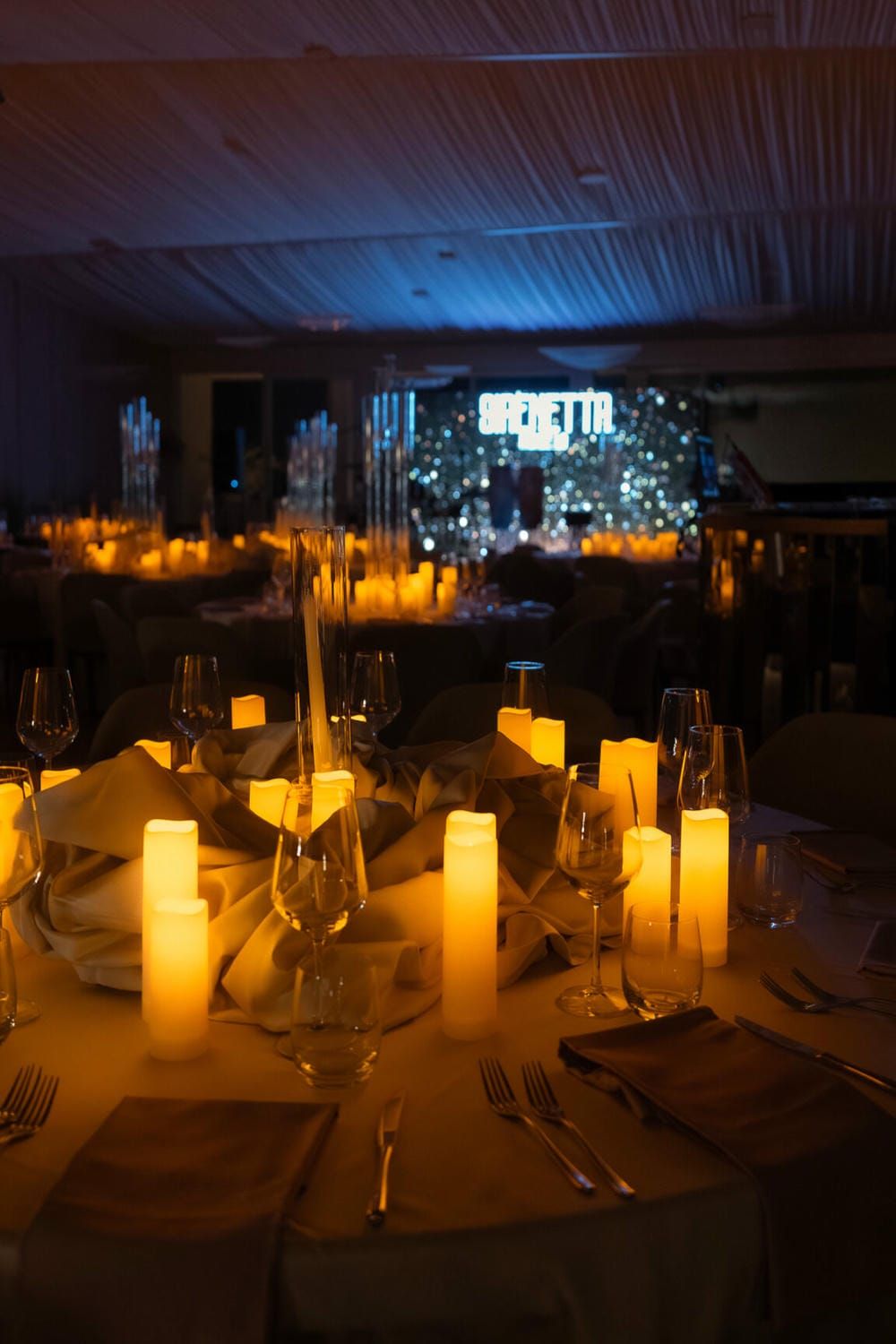 Elegant dining table set with glowing candles and wine glasses in a dimly lit romantic restaurant setting.
