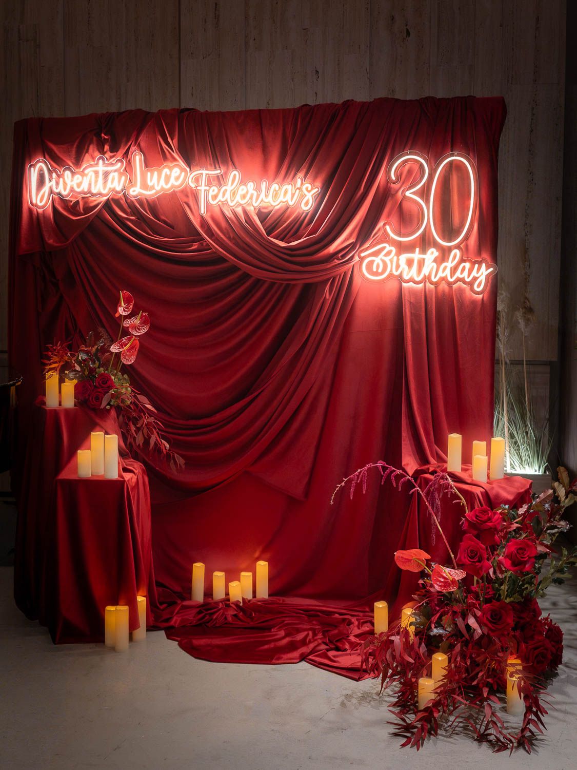 Editorial floral installation event with dramatic red velvet draping, glowing candles, and neon signage creating a romantic atmosphere.