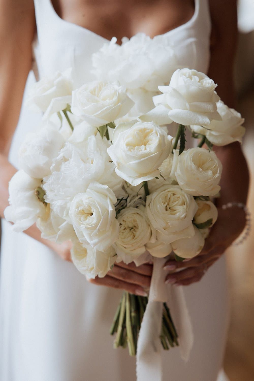 A delicate white rose wedding bouquet with satin ribbon wrap shown from multiple angles in soft natural light.