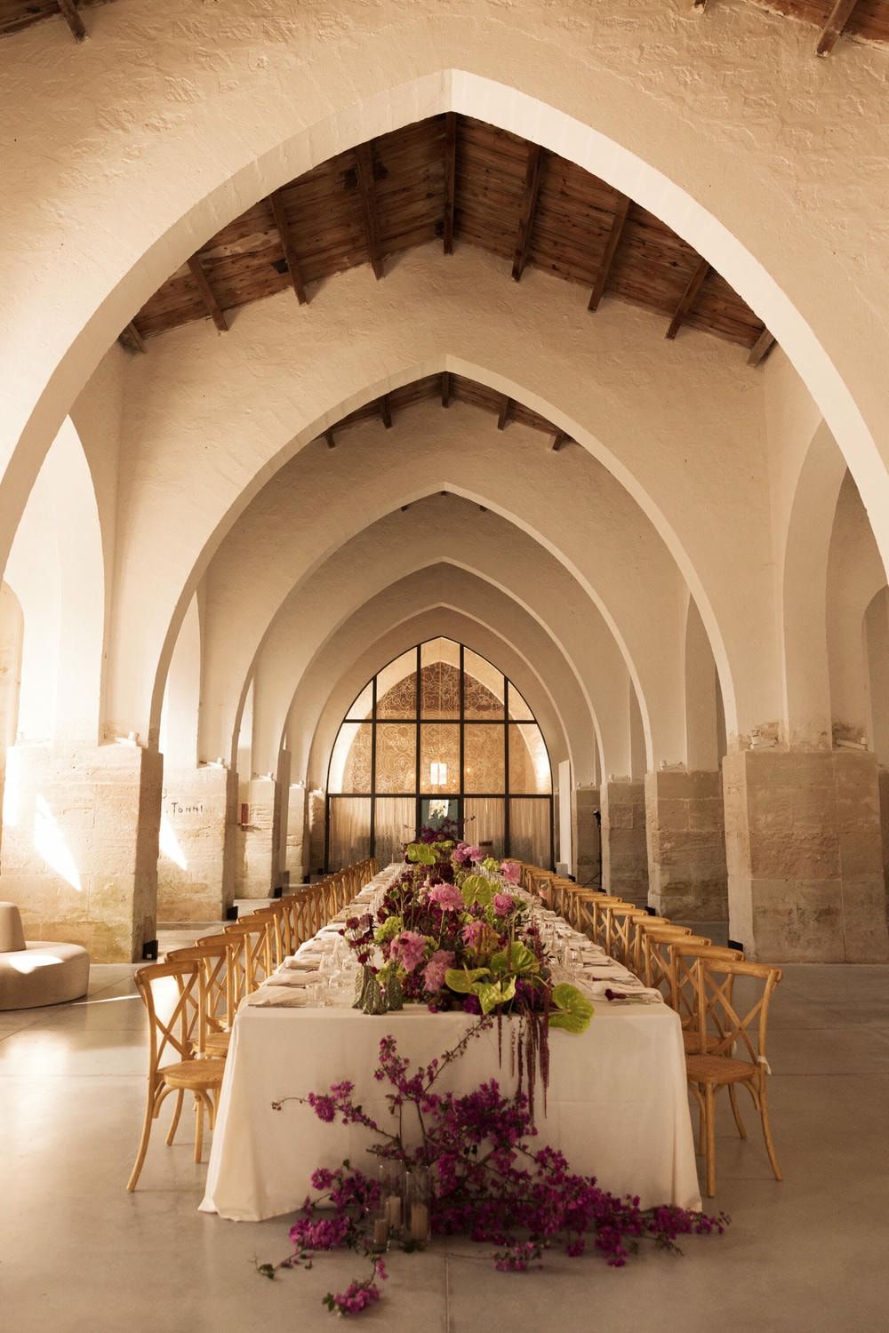 Elegant vaulted cellar venue with arched stone ceilings and tables decorated with purple floral arrangements.