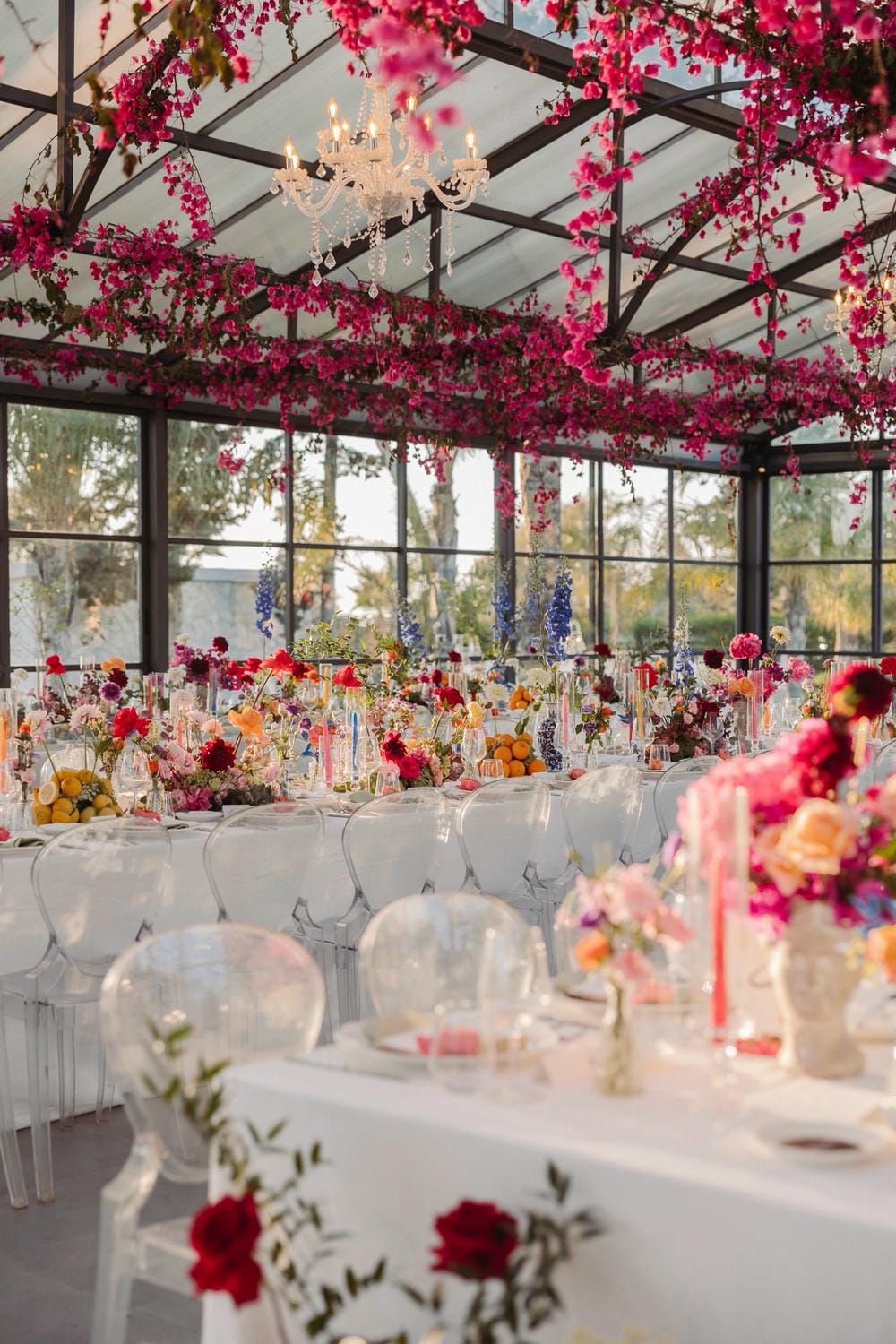 Elegant wedding reception venue with white tables and vibrant pink bougainvillea flowers hanging from glass ceiling.