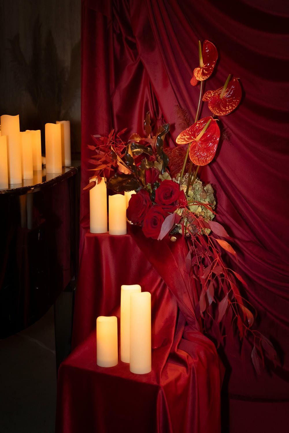Glowing white pillar candles arranged against deep red drapery with decorative butterflies and floral accents.