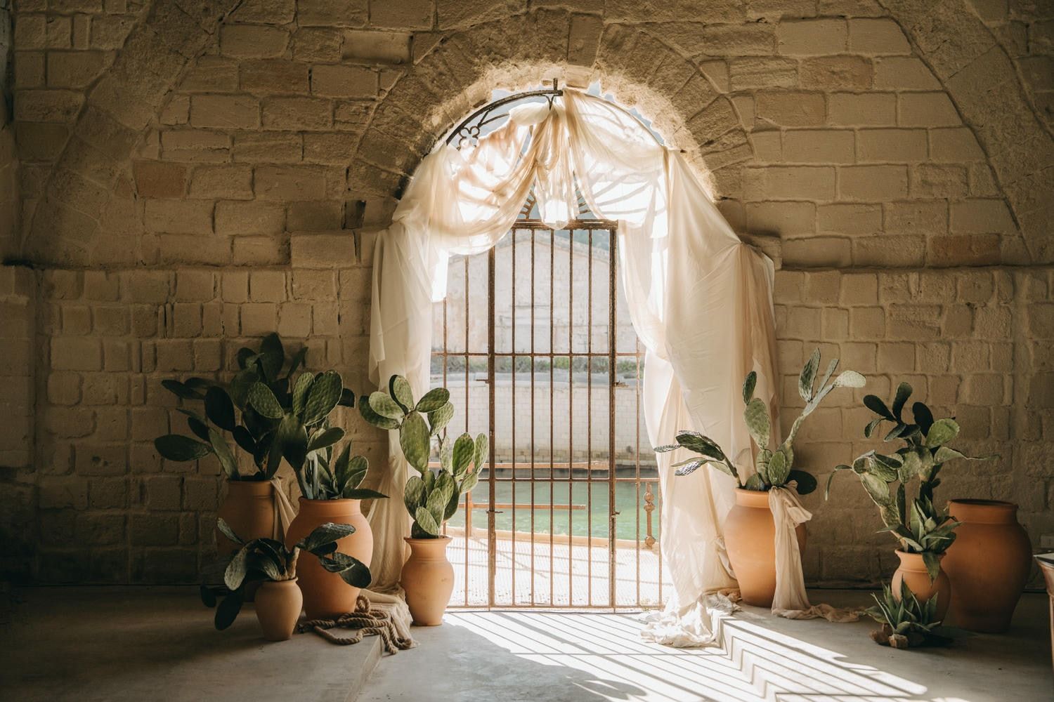 In Favignana a sunlit stone archway with terracotta pots and potted plants creates a rustic Mediterranean ambiance during wedding day.