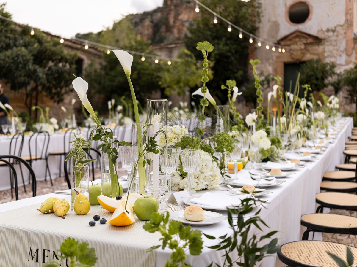 Elegant outdoor wedding reception table settings with white linens, greenery and citrus fruit centerpieces.