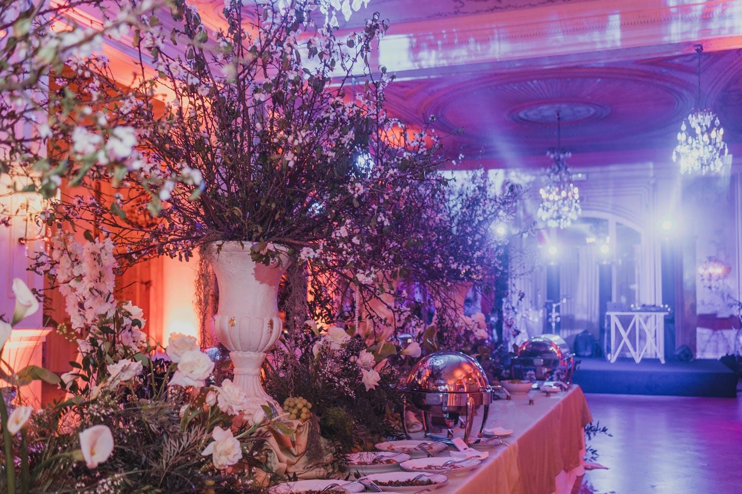 Elegant wedding reception at Villa Igiea decorated with purple and pink lighting, crystal chandeliers, and floral arrangements.