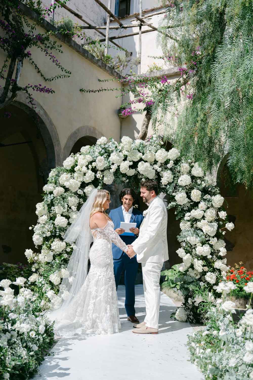 An outdoor wedding ceremony setup with white floral arches and cascading greenery creating an elegant garden atmosphere.