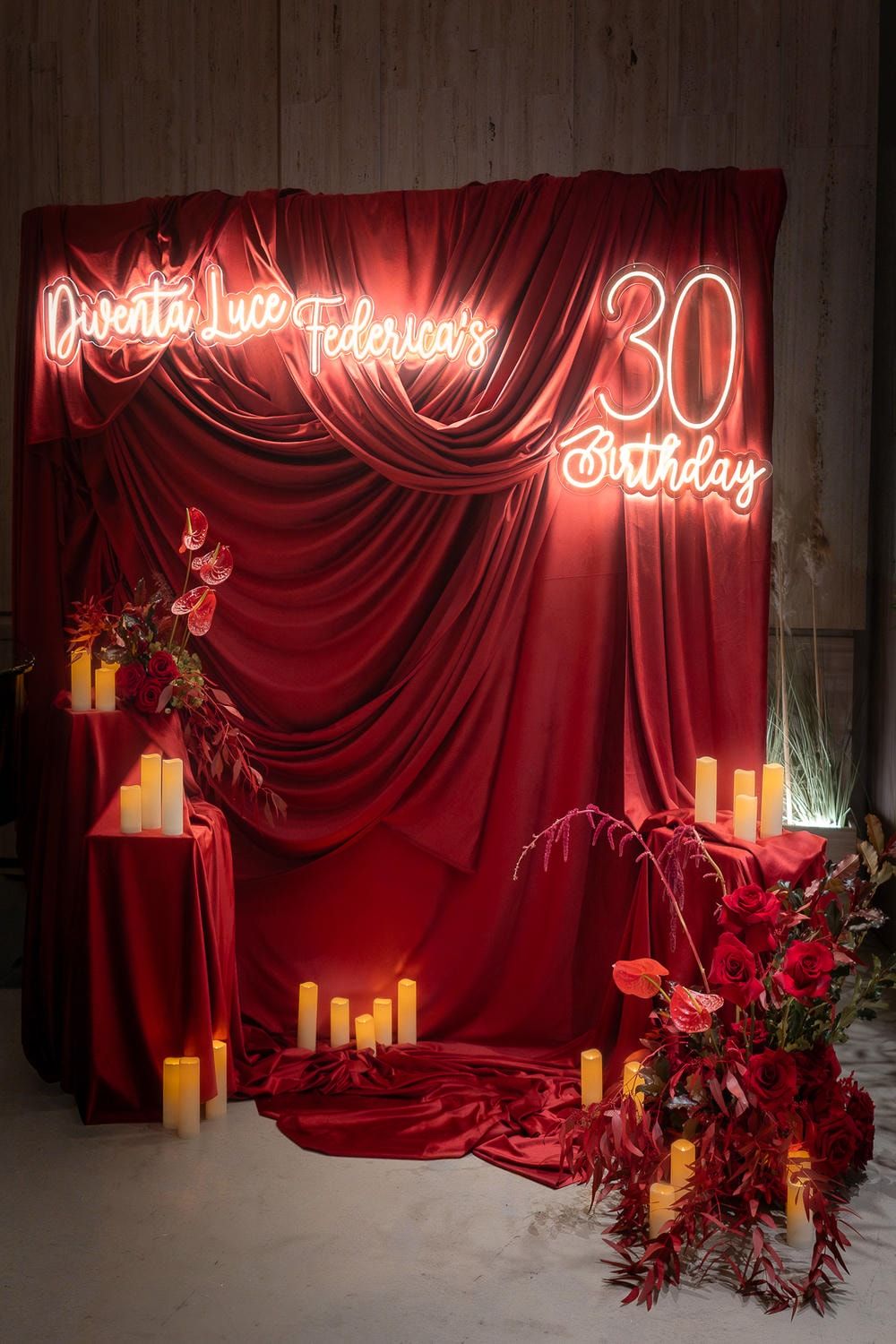 Red velvet curtain backdrop with glowing neon birthday text and illuminated candles creates an elegant party atmosphere.