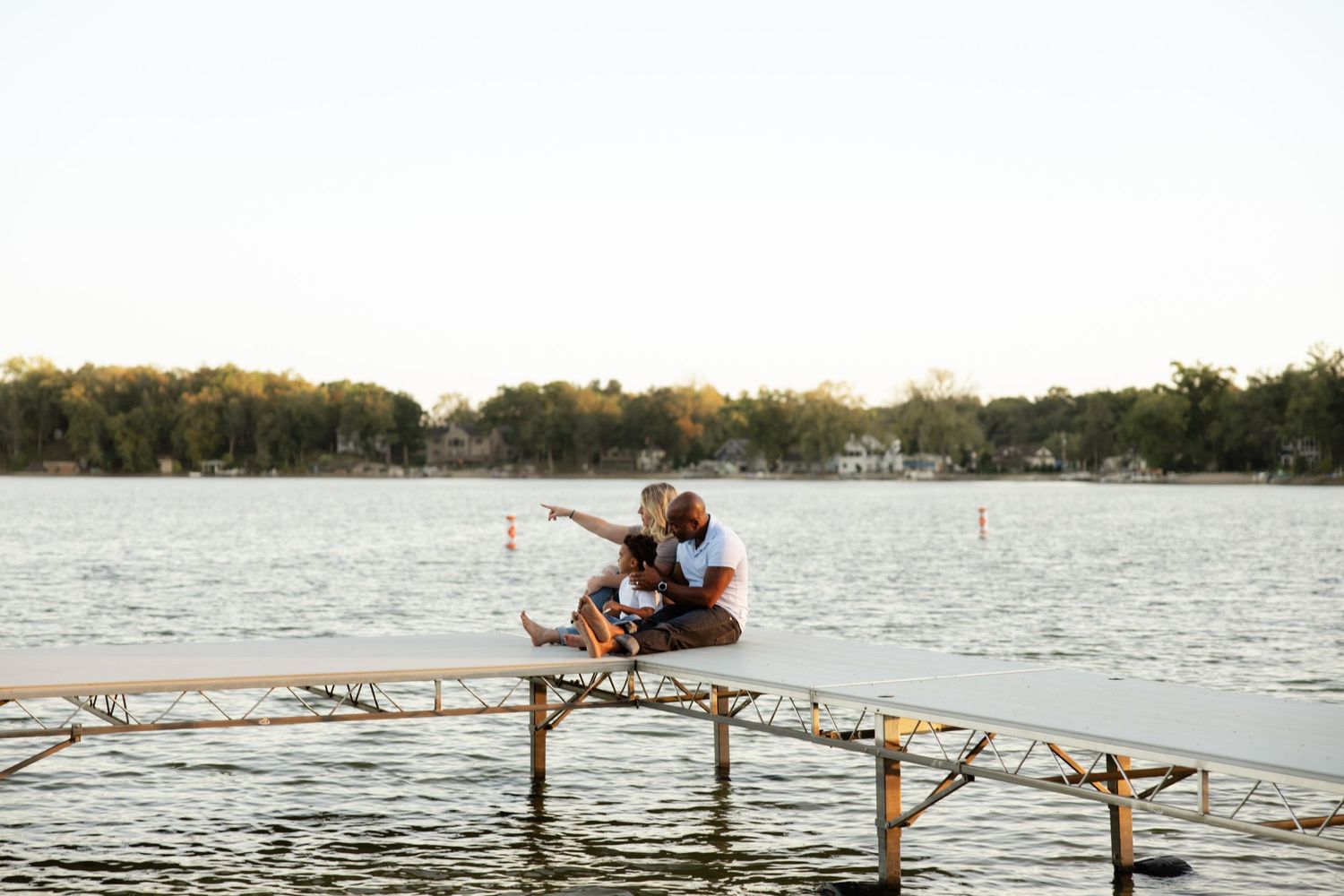A couple sits together on a wooden pier overlooking a serene lake at sunset.