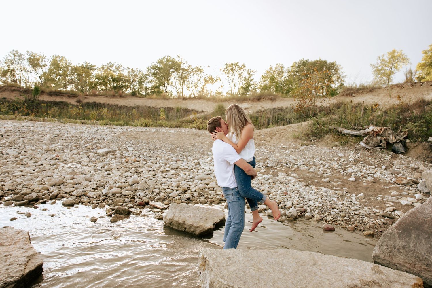 Couple sits together on rocky riverbank during sunset photoshoot.