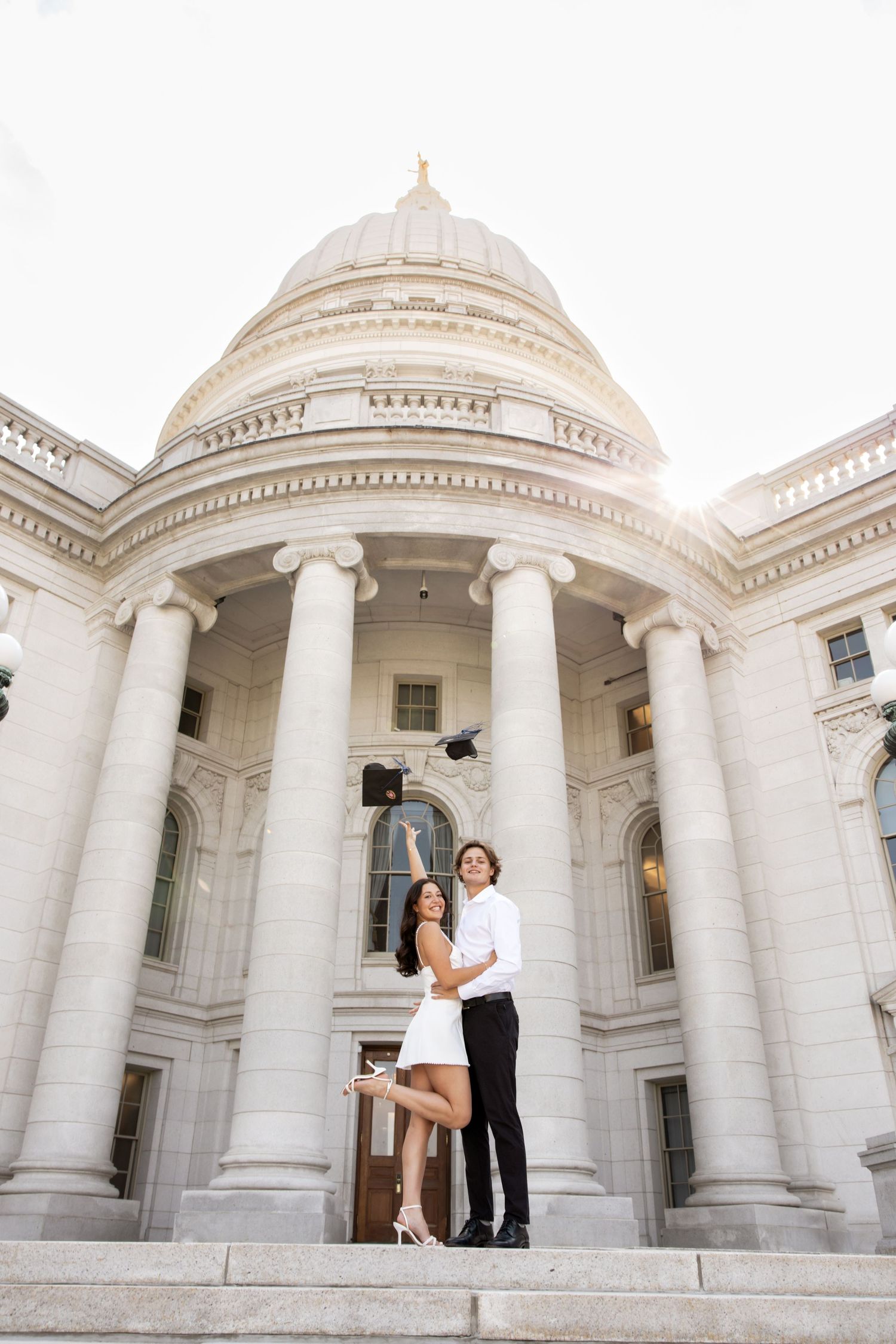 A couple poses on the steps of a grand neoclassical building with white columns and domed architecture.