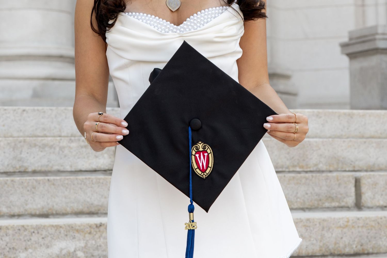 Close-up of graduation cap details with university logo and tassel against white dress.