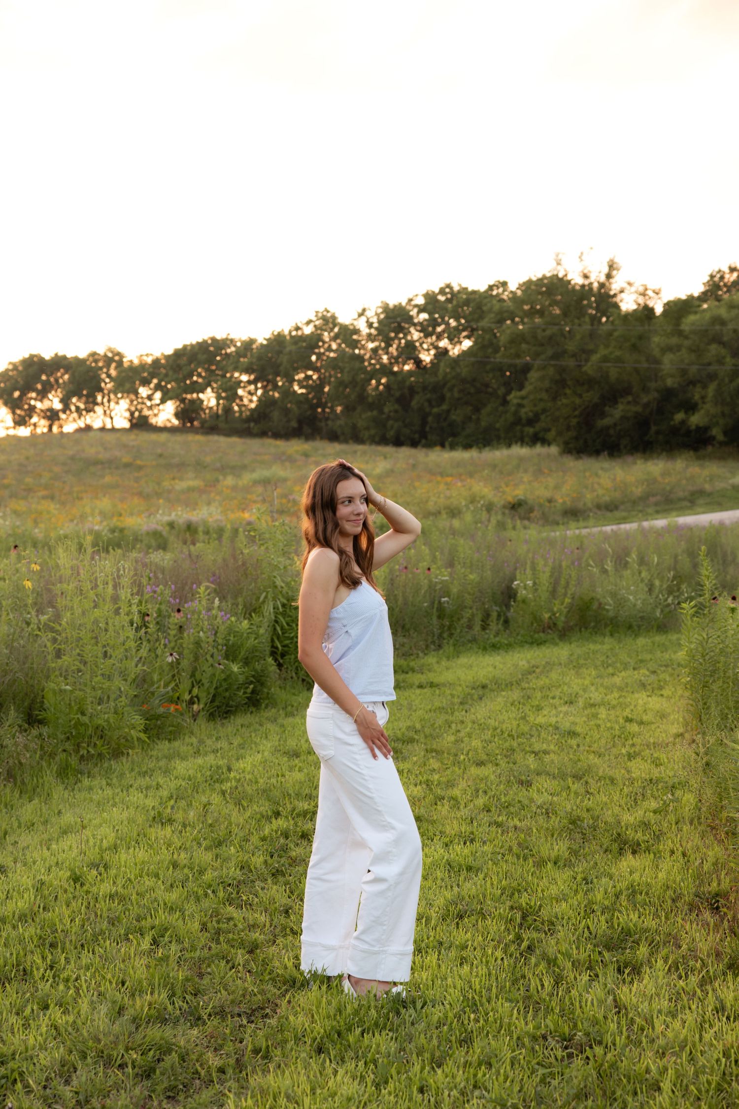 Woman in flowing white dress twirls in a summer meadow at golden hour.