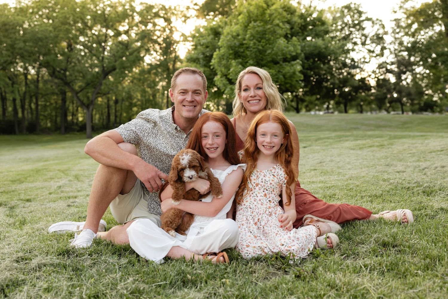 Family relaxing together on grassy hill during summer evening.