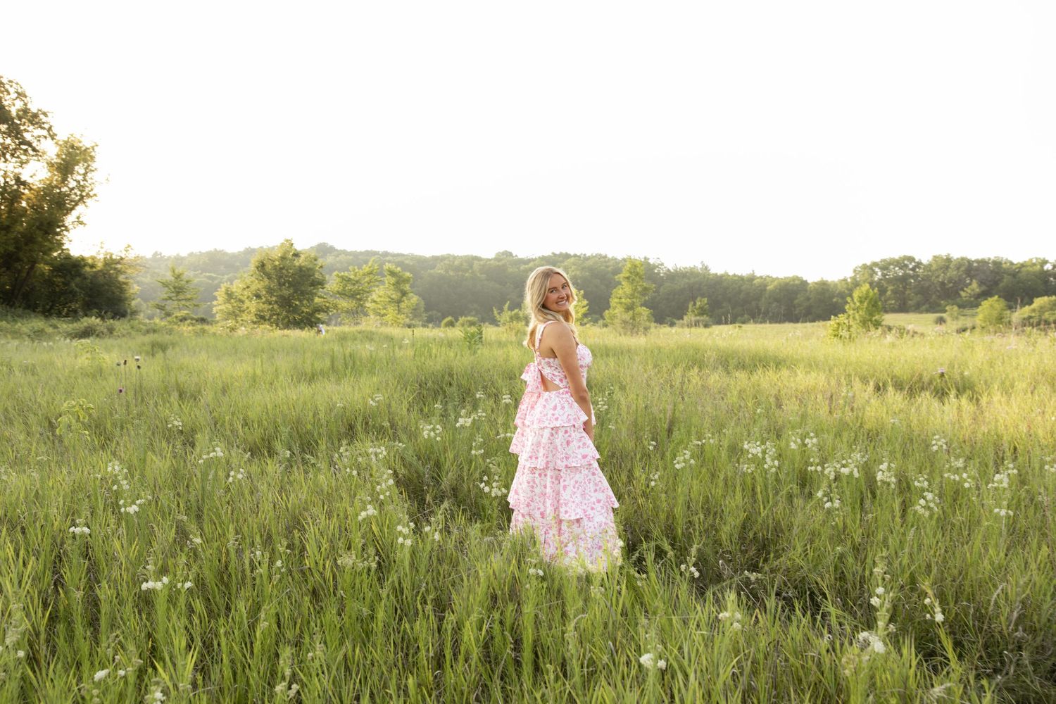 A figure in a flowing dress poses gracefully in a golden summer field at sunset.