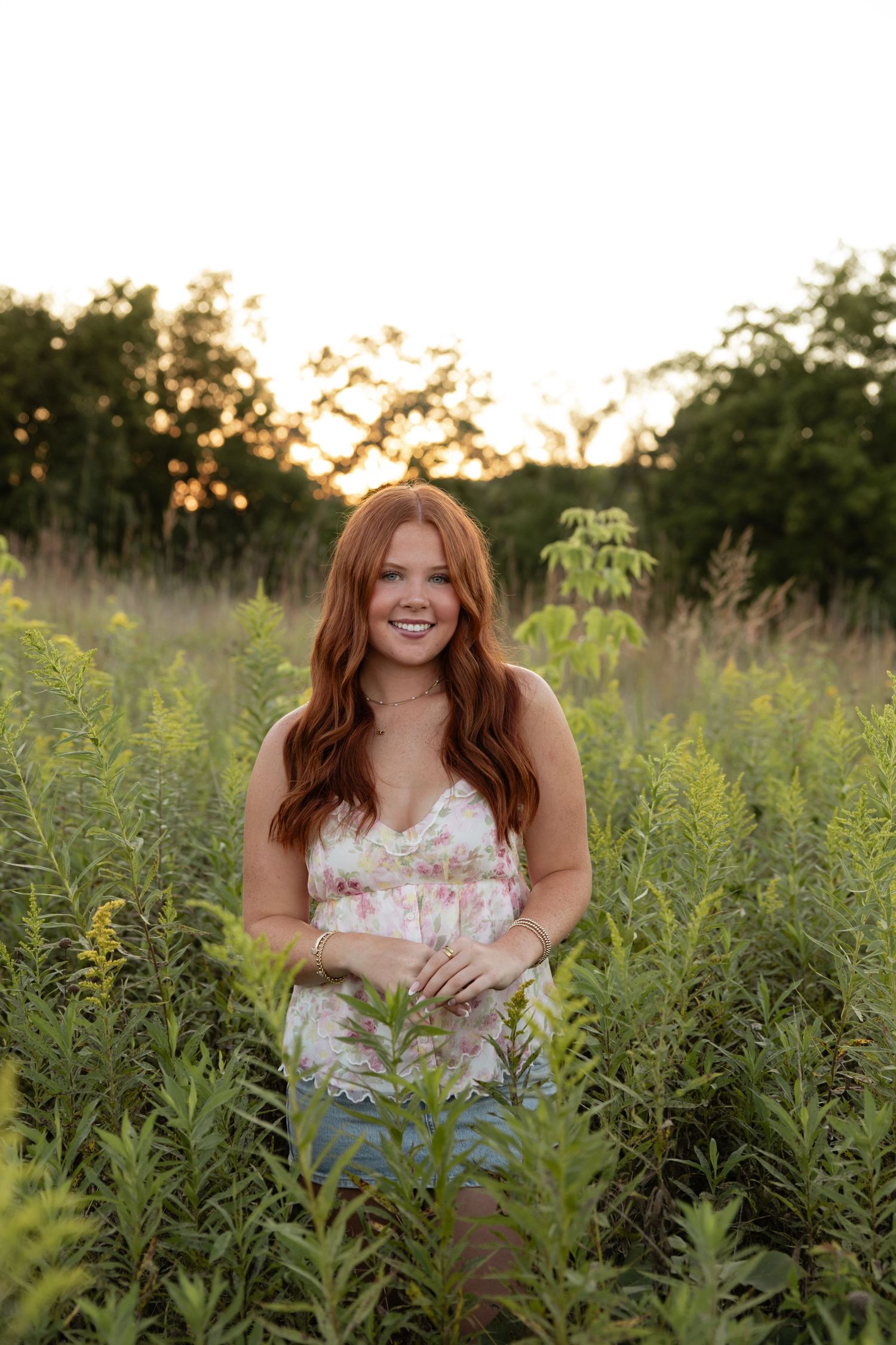 Person sitting in a wildflower field wearing a floral dress at sunset.